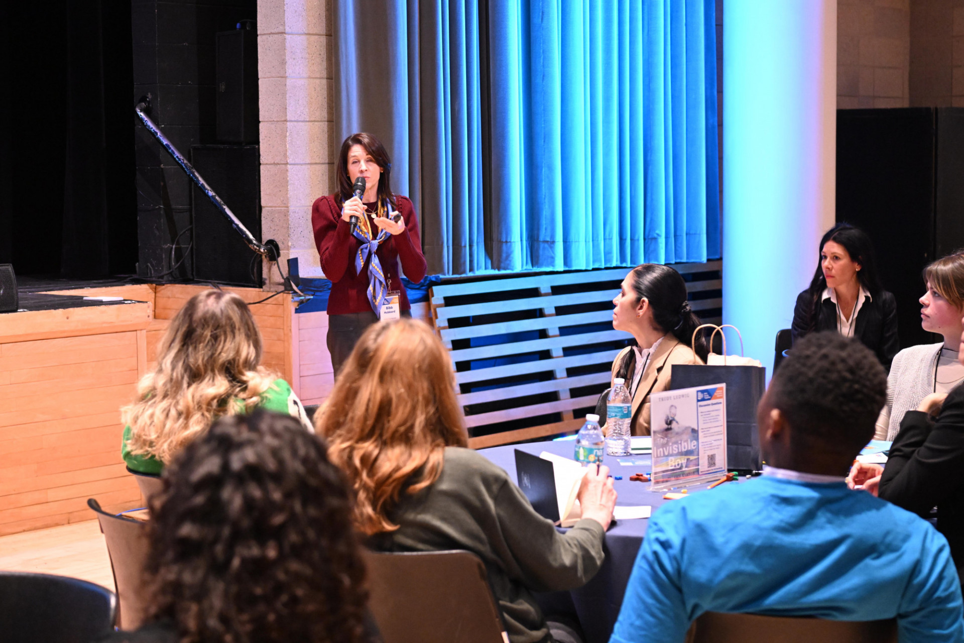 a woman speaking into a microphone in front of a group seated at tables