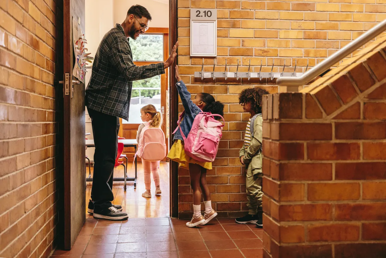 teacher high fives young students as they enter the classroom. 