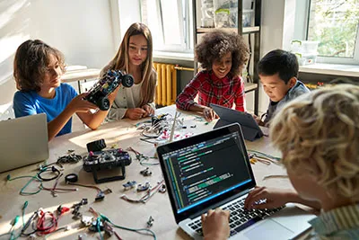 Kids working together with laptops and other materials. 