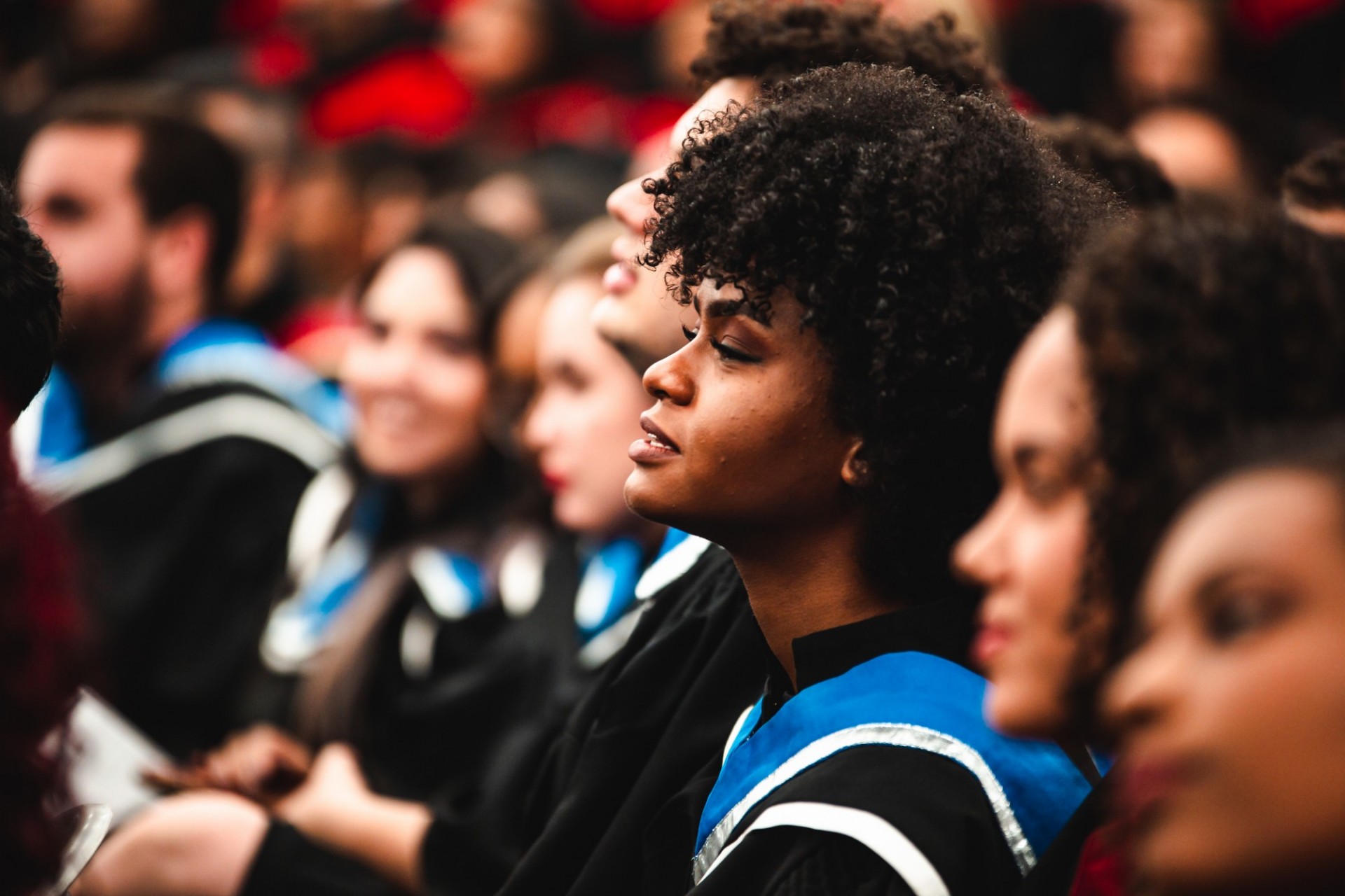 College aged black female wearing graduation robes alongside her graduating peers