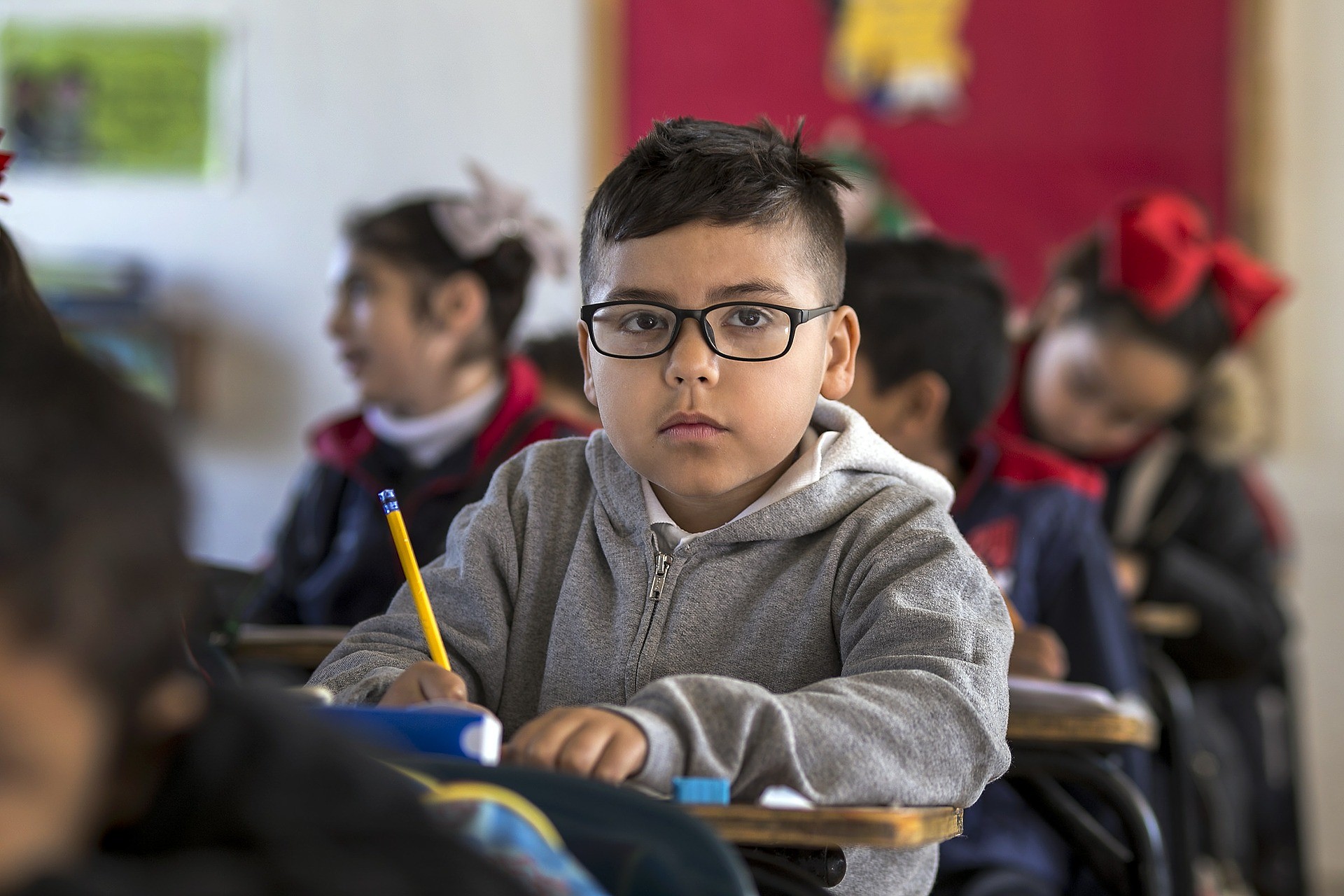 Elementary aged Latino student seated in a classroom surrounded by his peers with a pencil in hand